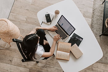 Overhead view of a woman using a laptop at a home desk, surrounded by books, a , and a cup. HD wallpaper