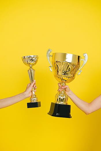 Two hands holding trophies against a vivid yellow backdrop, symbolizing success. HD phone wallpaper