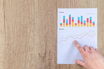 Hand analyzing business graphs on a wooden desk, focusing on data results and growth analysis. HD wallpaper