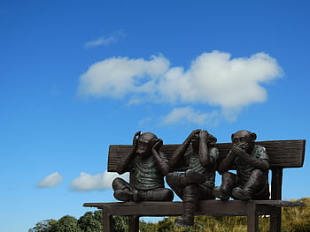 Artistic sculpture depicting the Three Wise Monkeys on a bench outdoors against blue sky. HD wallpaper