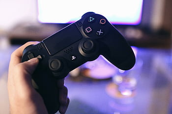 Person holding a gaming controller, blurred screen in background. HD wallpaper
