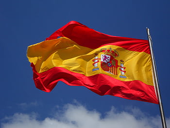Vibrant Spanish flag waving against a clear blue sky and clouds. HD wallpaper