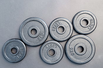 Close-up of steel gym weight plates in various sizes arranged on a gray surface. HD wallpaper