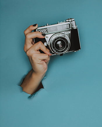 A hand holds a classic vintage camera through a torn blue paper background. HD phone wallpaper