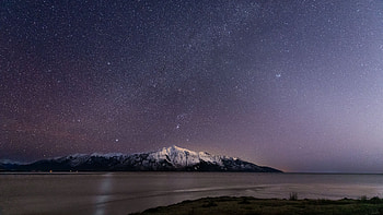 Landscape View Of Snow Capped Rock Mountain Under Starry Sky Ocean Water Dark Background HD wallpaper