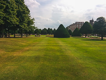 Beautiful landscaped garden with topiary near a historic mansion, under a cloudy sky. HD wallpaper
