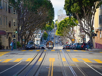 A vibrant city street in San Francisco featuring a classic cable car and iconic architecture. HD wallpaper