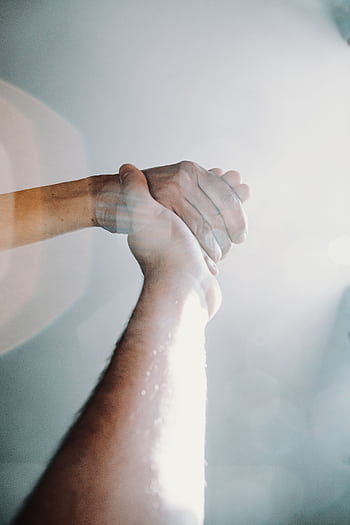 Two hands clasped, symbolizing unity and support with a bright, ethereal background. HD phone wallpaper