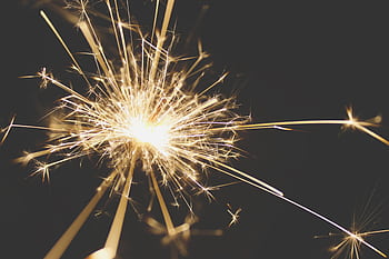 Close-up of a dazzling sparkler bursting with light against a dark background, perfect for celebrations. HD wallpaper