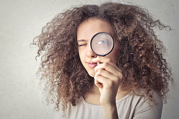 Close-up portrait of a woman winking and holding a magnifying glass against a white background. HD wallpaper