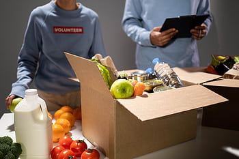 People packing a cardboard box with essentials like fruits, vegetables, and bottled water for charity. HD wallpaper
