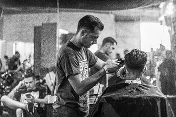 A barber skillfully gives a haircut in a stylish Wrocław barbershop, captured in moody monochrome. HD wallpaper