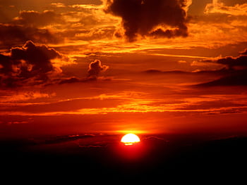 Vivid sunset with a glowing sun on the horizon and dramatic clouds, casting warm tones. HD wallpaper
