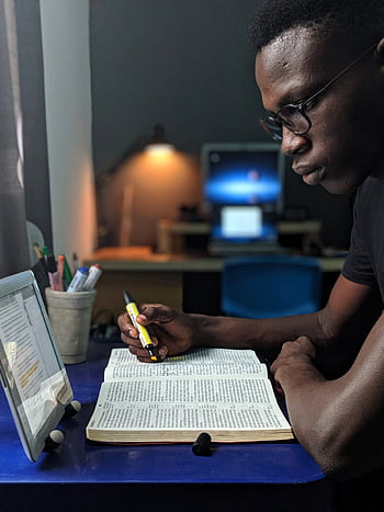 Man deeply engaged in studying with a book and tablet at a desk HD phone wallpaper