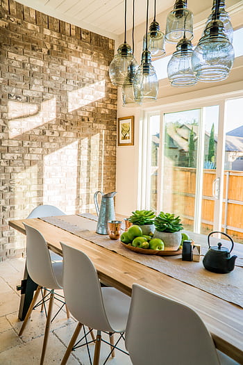 Sunlit dining room with contemporary decor and a rustic brick wall, featuring stylish lighting and a wooden table. HD phone wallpaper