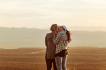 Two women share a romantic kiss against a stunning sunset backdrop, embracing love and togetherness. HD wallpaper