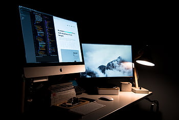 A clean and stylish workspace featuring dual monitors, a lamp, and office supplies. HD wallpaper