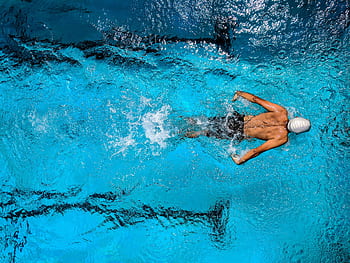 Top view of a swimmer wearing a cap, performing a front crawl stroke in a clear blue swimming pool. HD wallpaper