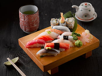 Elegant display of sushi with green tea on a wooden board, capturing authentic Japanese cuisine. HD wallpaper