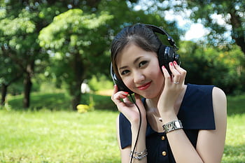 Smiling young woman listening to music with heads in a sunny park. HD wallpaper