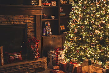 Warm holiday scene of a decorated Christmas tree with gifts by a cozy fireplace. HD wallpaper