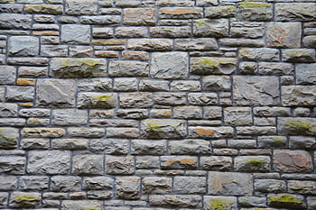 Close-up of a textured stone wall with moss, showcasing natural patterns and rugged appeal. HD wallpaper