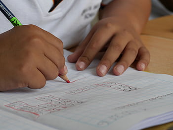 Close-up of a student writing math equations in a notebook with a pencil indoors. HD wallpaper