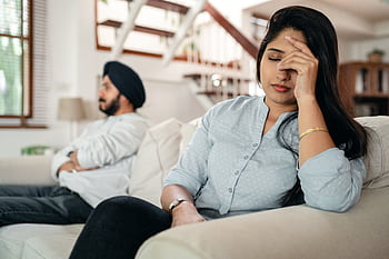 A young couple sitting on a couch indoors, showing signs of stress and frustration. HD wallpaper