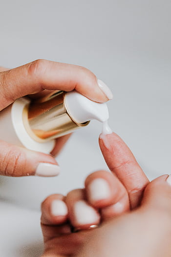 A woman applies skincare lotion from a pump bottle, showcasing manicured nails. HD phone wallpaper