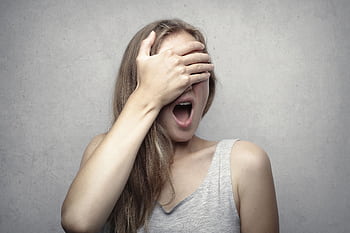 A surprised woman covers her face with one hand, expressing shock and amazement against a gray background. HD wallpaper