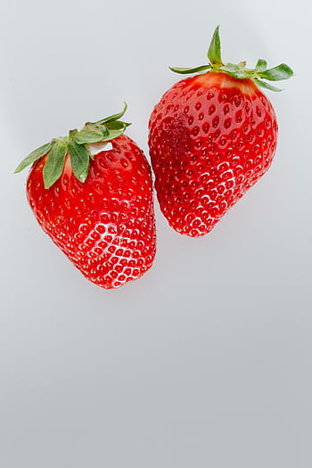 Two ripe strawberries with vibrant red color on a white background, showcasing freshness. HD phone wallpaper