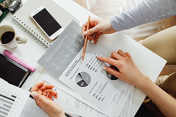 Team collaborating on financial documents with graphs and statistics in an office setting. HD wallpaper