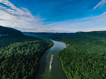 Aerial shot of a barge navigating a winding river through lush green forests under a clear blue sky. HD wallpaper