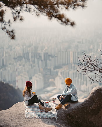 Couple enjoying a scenic picnic with a breathtaking view of the Seoul skyline from a mountain cliff. HD phone wallpaper