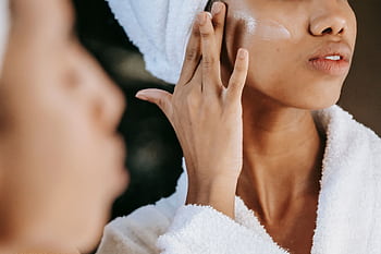 A close-up of an ethnic woman applying moisturizing cream on her face with a blurred reflection in the mirror. HD wallpaper