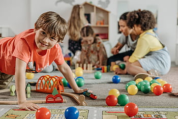Happy children and a caregiver playing with colorful toys in a lively indoor playroom setting. HD wallpaper