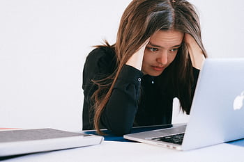 A stressed woman at a desk, looking at a laptop with a worried expression. HD wallpaper
