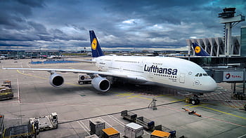 Lufthansa Airbus A380 parked at the airport gate, ready for departure under a dramatic cloudy sky. HD wallpaper