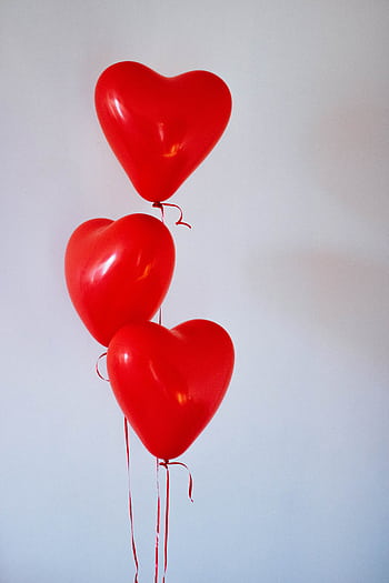Three red heart-shaped balloons floating in a minimalist studio setting, evoking love and romance. HD phone wallpaper