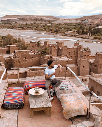 Man enjoying tea on a rooftop terrace overlooking Ait Benhaddou, Morocco. HD phone wallpaper