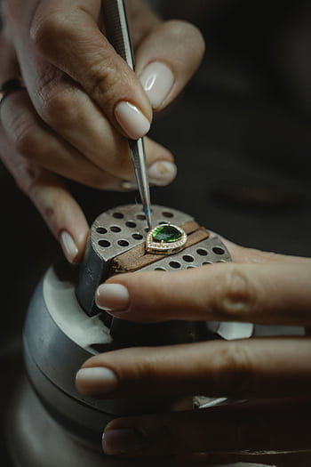 A skilled jeweler carefully crafting an emerald ring using a tweezer, showcasing craftsmanship. HD phone wallpaper