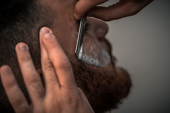 Detailed close-up of a barber using a razor for precise beard trimming in the barbershop. HD wallpaper