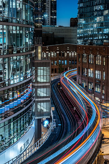 Long exposure of urban train tracks creating vibrant light trails in a modern cityscape at night. HD phone wallpaper