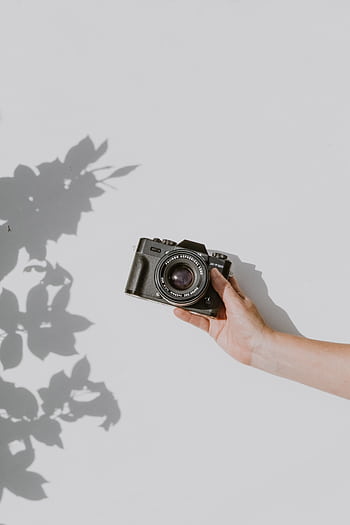 A hand holds a vintage camera against a white background, casting a shadow. HD phone wallpaper