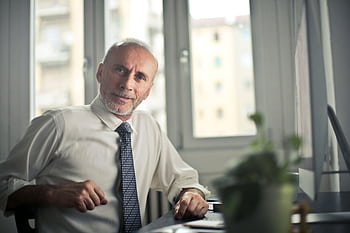 A mature man in professional attire smiling in an office setting. HD wallpaper