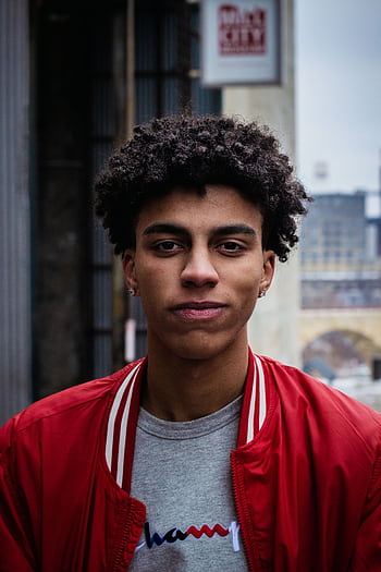 Portrait of a young man in a red jacket, captured in an urban setting with a solemn expression. HD phone wallpaper