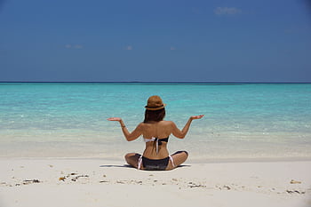 A woman meditating on a serene beach in the Maldives, under a clear blue sky. HD wallpaper