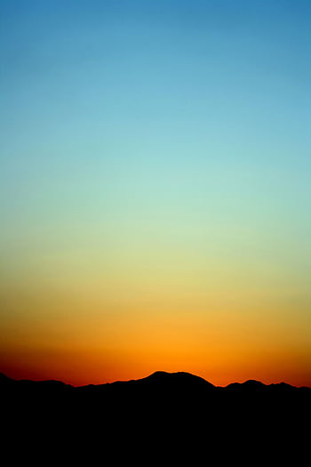 A stunning sunset creates a silhouette of distant mountains under a vivid gradient sky. HD phone wallpaper