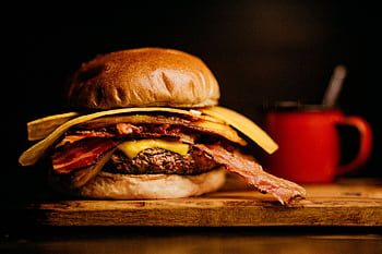 Close-up of a gourmet bacon cheeseburger with a side of crispy fries on a wooden board. HD wallpaper