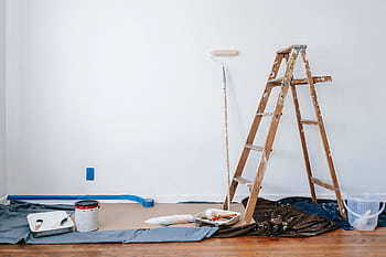 A room prepared for renovation with a ladder, paint supplies, and drop cloth. HD wallpaper